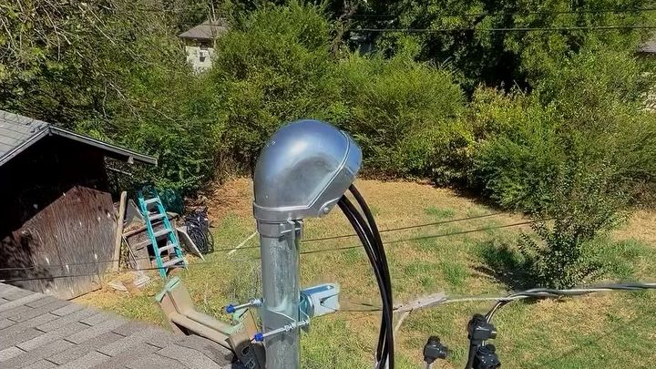 A new service riser on a shingle roof, a shed, a yard and trees beyond.