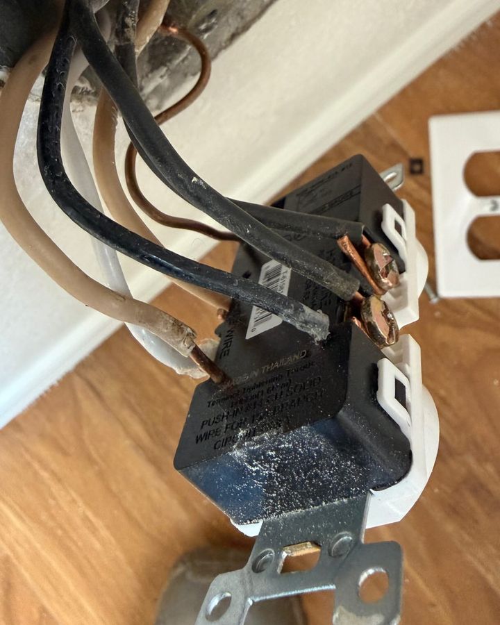 The wiring behind an open receptacle box: black and white conductors landed on a device pulled from the wall.